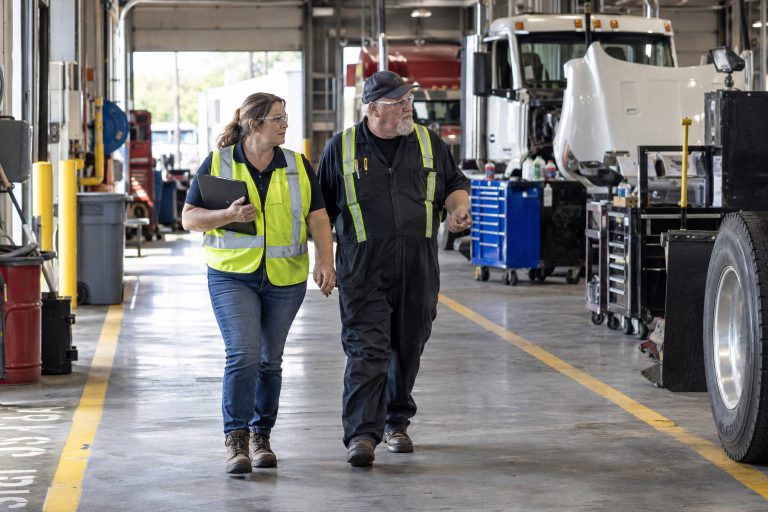 Two people in high-visibility vests walking through a maintenance shop