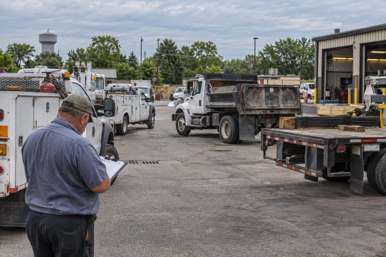A vocational fleet of dump and service trucks with a person holding a clipboard in the foreground